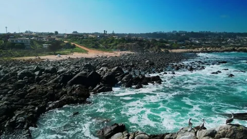 Backward flight above dark boulder-covered shoreline with turquoise waves Stock-Footage 332685887