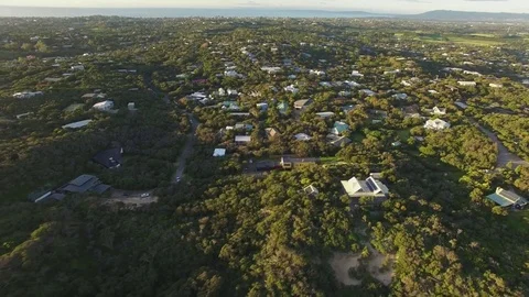Backward flight away from rural houses among coastal vegetation at sunset. Mo Stock Footage