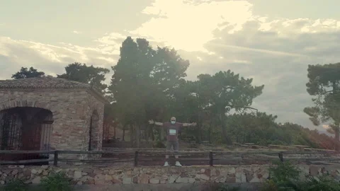 Backward flight of drone flying over backlit man flying off cliff Stock Footage 138896016