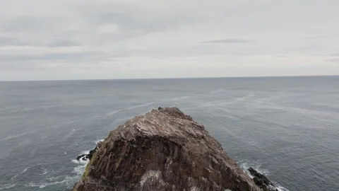 Backwards reveal drone shot of Bow Fiddle Rock on an overcast day along the Stock Footage 334813718