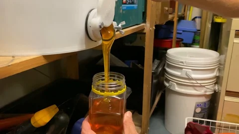 Backyard bee keeper fills jar with harvested honey from a large tub Stock Footage 129289924