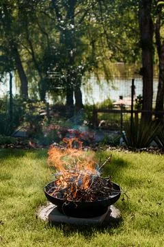 Backyard Fire Pit Scene: Warm Flames in Green Landscape, Lake View, Rustic .. Stock Photos