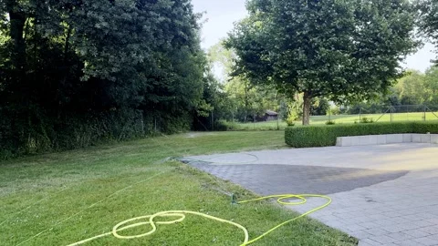 Backyard Garden with Coiled Hoses and Sprinkler Watering Lawn in Summer Stock Footage 340238484