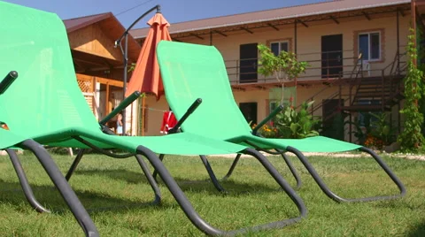 Backyard patio area of small tourist hotel with green sun loungers on grass lawn Stock Footage