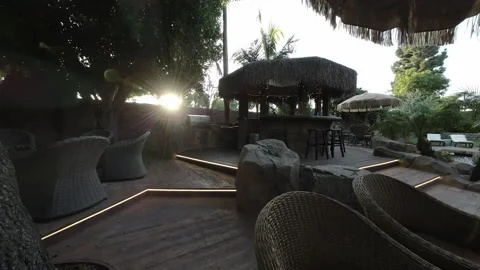 Backyard patio dining table and thatched tiki bar at sunset Stock Footage 345542504