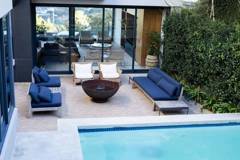 Backyard patio featuring circular fire pit with navy and white chairs Stock Photos