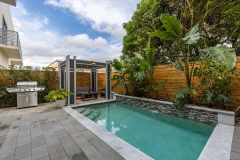 Backyard Surrounded by large vegetation short grass and blue pool Stock Photos