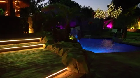 Backyard swimming pool lit blue at dusk with glowing steps and trees Stock Footage 345541336