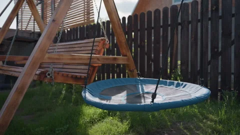 Backyard swing set with round nest swing and wooden bench under sunlight Stock Footage 316841526