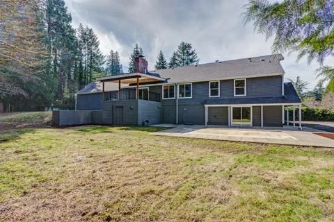 Backyard view of Gray home with covered deck on the second level and spacious Stock Photos