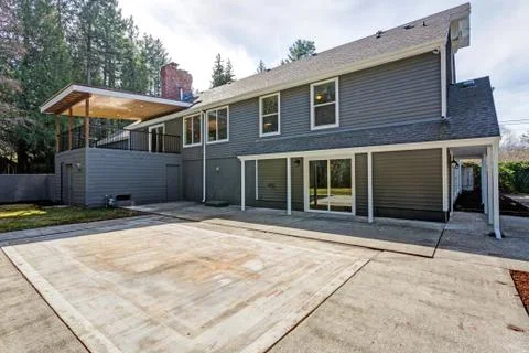 Backyard view of Gray home with spacious patio area and concrete floor. Stock Photos