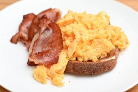 Bacon and scrambled egg with slice of toast on a white plate Stock Photos