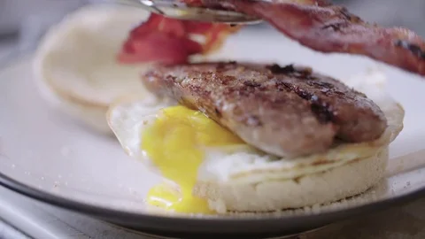 Bacon being placed onto breakfast muffin with egg and sausage Stock Footage 85307405