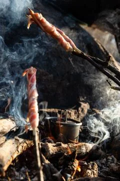 Bacon being roasted on sticks over open fire while water is heated for tea Stock Photos