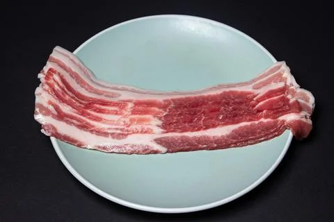 Bacon on a black background. Raw bacon on a plate.  Stock Photos