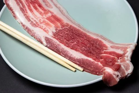 Bacon on a black background. Raw bacon on a plate. Chinese sticks next to pieces Stock Photos