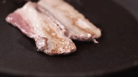 Bacon is fried in a pan, smoke and grease splashes. Close-up. Stock Footage 146335151