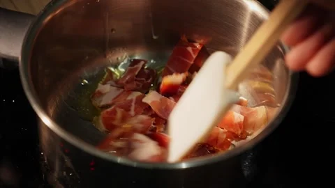 Bacon frying in pan while being stirred with wooden spoon Stock Footage 312343789