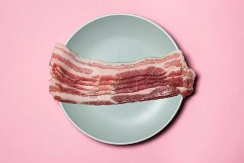 Bacon on a pink background. Raw bacon on a plate. Stock Photos