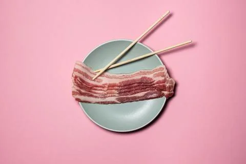 Bacon on a pink background. Raw bacon on a plate. Chinese sticks next to pieces  Stock Photos