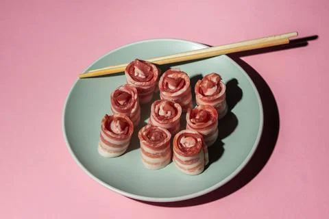 Bacon on a pink background. Raw bacon on a plate. Chinese sticks next to pieces  Stock Photos