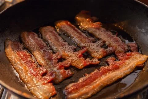 Bacon strips or rashers cooked in frying pan in the rays of sunlight Stock Photos