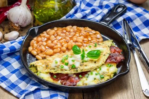 Bacon stuffed omelette with backed beans on a iron cast pan Foto stock