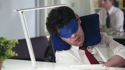 Badly tired man sleeping at work in sleep mask and neck pillow Stock Footage 93984260