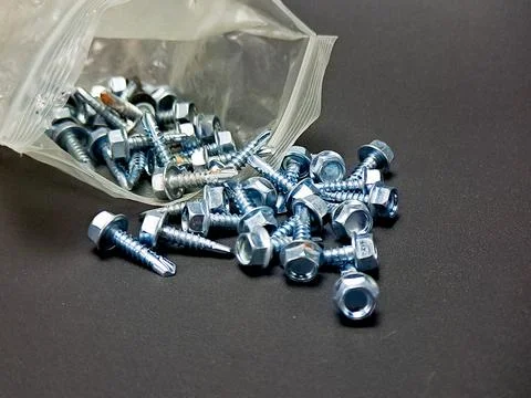 Bag of shiny hexagonal head screws spills out across a matte gray surface i.. 스톡 사진