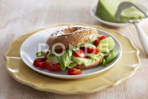 A Bagel With Pesto Cheese, Cherry Tomatoes And Basil