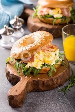 Bagels with scrambled eggs, rucola and fried bacon Stock Photos