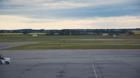 A Baggage Handler drives a long empty luggage vehicle across barren tarmac. Video stock 88190084