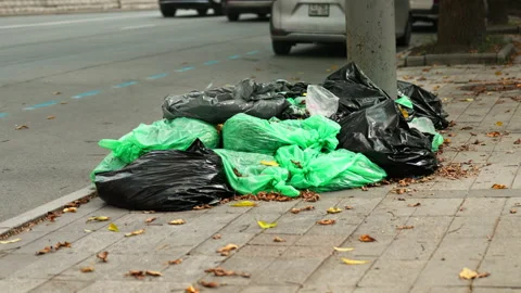 Bags of trash are lying in the middle of a city street. Cars drive past. En.. Stock-Footage 346318464