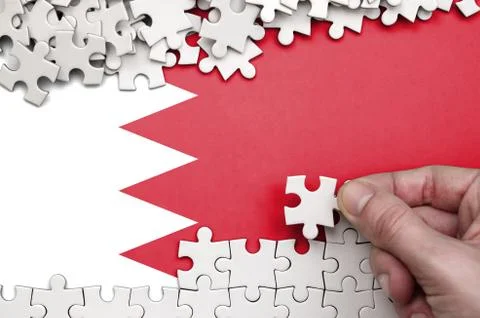 Bahrain flag  is depicted on a table on which the human hand folds a puzzle o Foto stock