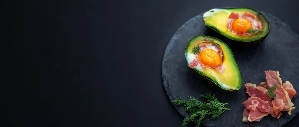 Baked avocado with an egg on a black background and copy space Stock Photos
