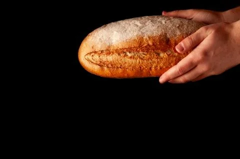 Baked bread on a black background in hands 库存照片