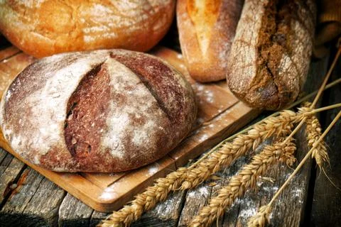 Baked bread of different types and shapes and wheat ears on the wooden boards Foto stock