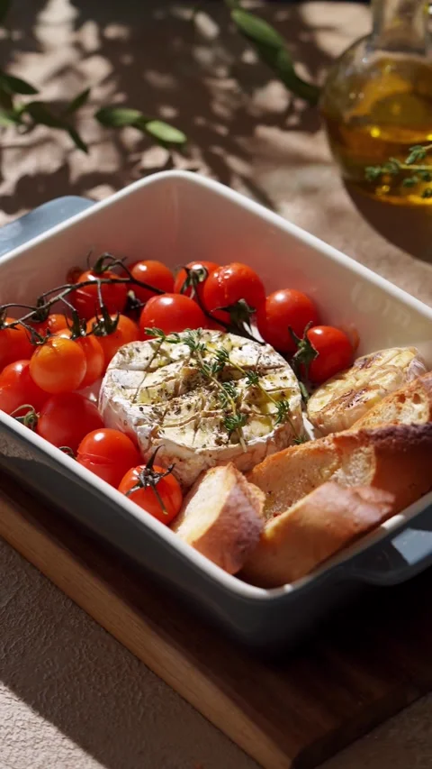 A baked Camembert cheese in a dish surrounded by cherry tomatoes on the vine, Stock Footage 330616413