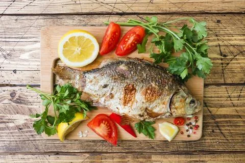 Baked carp fish with vegetables and spices on a wooden table. Stock-Fotos