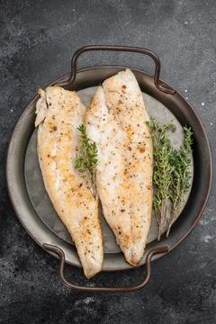 Baked cod style fish fillet, seasoned and herbed, served in iron pan on woo.. Stock Photos
