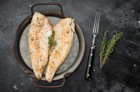 Baked cod style fish fillet, seasoned and herbed, served in iron pan on woo.. Stock Photos
