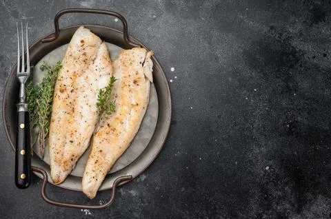 Baked cod style fish fillet, seasoned and herbed, served in iron pan on woo.. Stock Photos