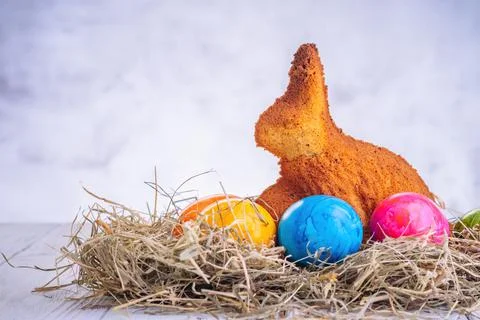 Baked easter bunny and easter decorated eggs on straw on wooden background Foto stock