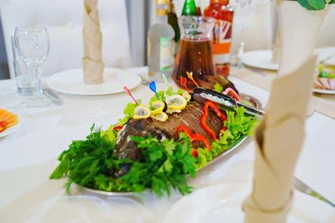 Baked fish on a platter with greens and lemon. Stock Photos