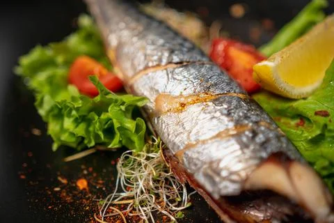 Baked fish without head with tomatoes, lettuce, microgreens, spices  Stock Photos