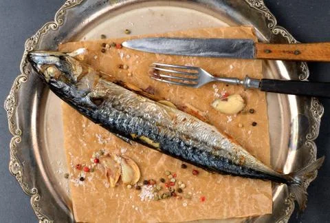 Baked mackerel with garlic, pepper and coarse salt on baking paper, knife and Stock Photos