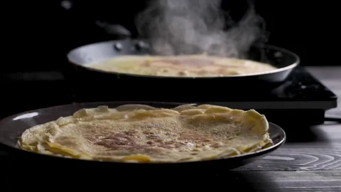 Baked pancake on foreground, background pan with baking pancake slow motion Stock Footage 169237216