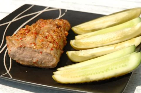 Baked pork meat and cucumbers on plate Stock Photos