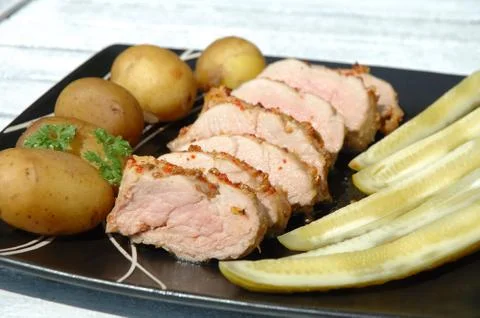 Baked pork meat, potatoes and cucumbers on plate Stock Photos