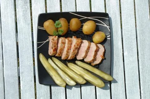 Baked pork meat, potatoes and cucumbers on plate Stock Photos